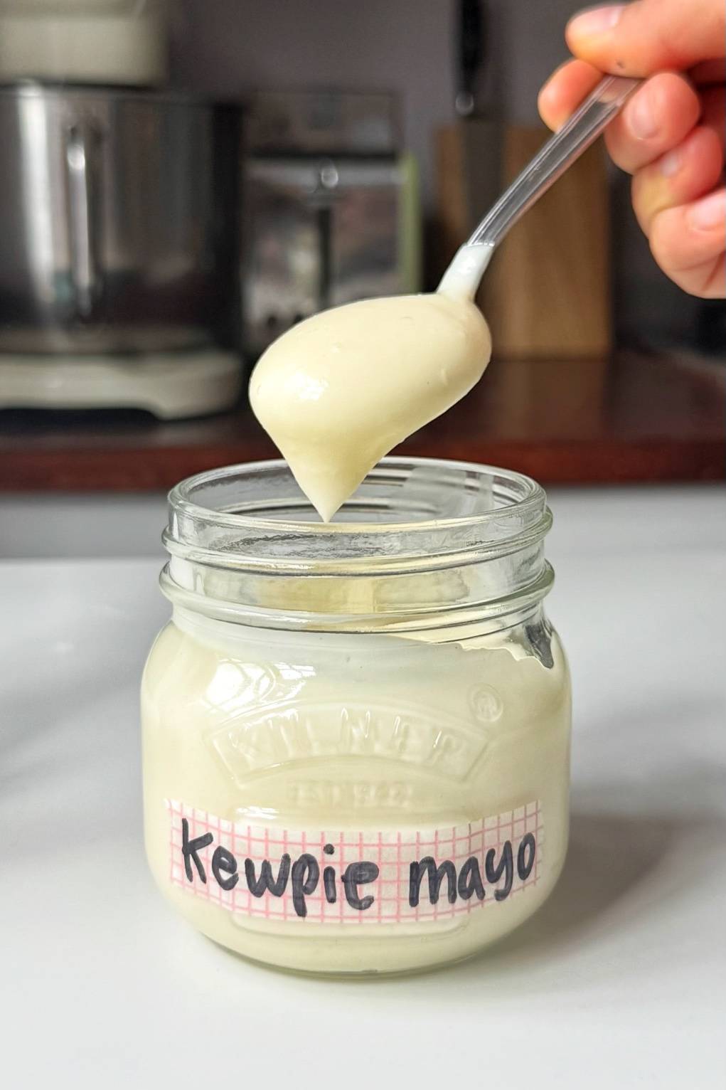 A spoonful of thick, creamy homemade kewpie mayo lifted from a glass jar showing the smooth texture.