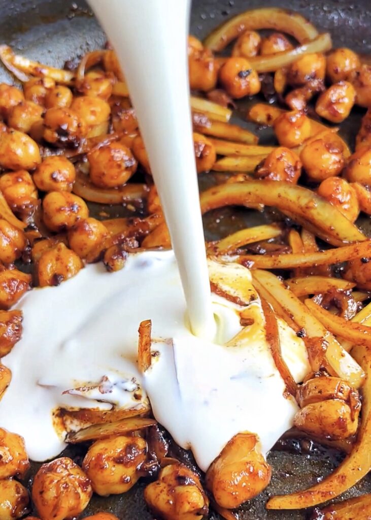 pouring single cream into a pan of chickpeas and onion