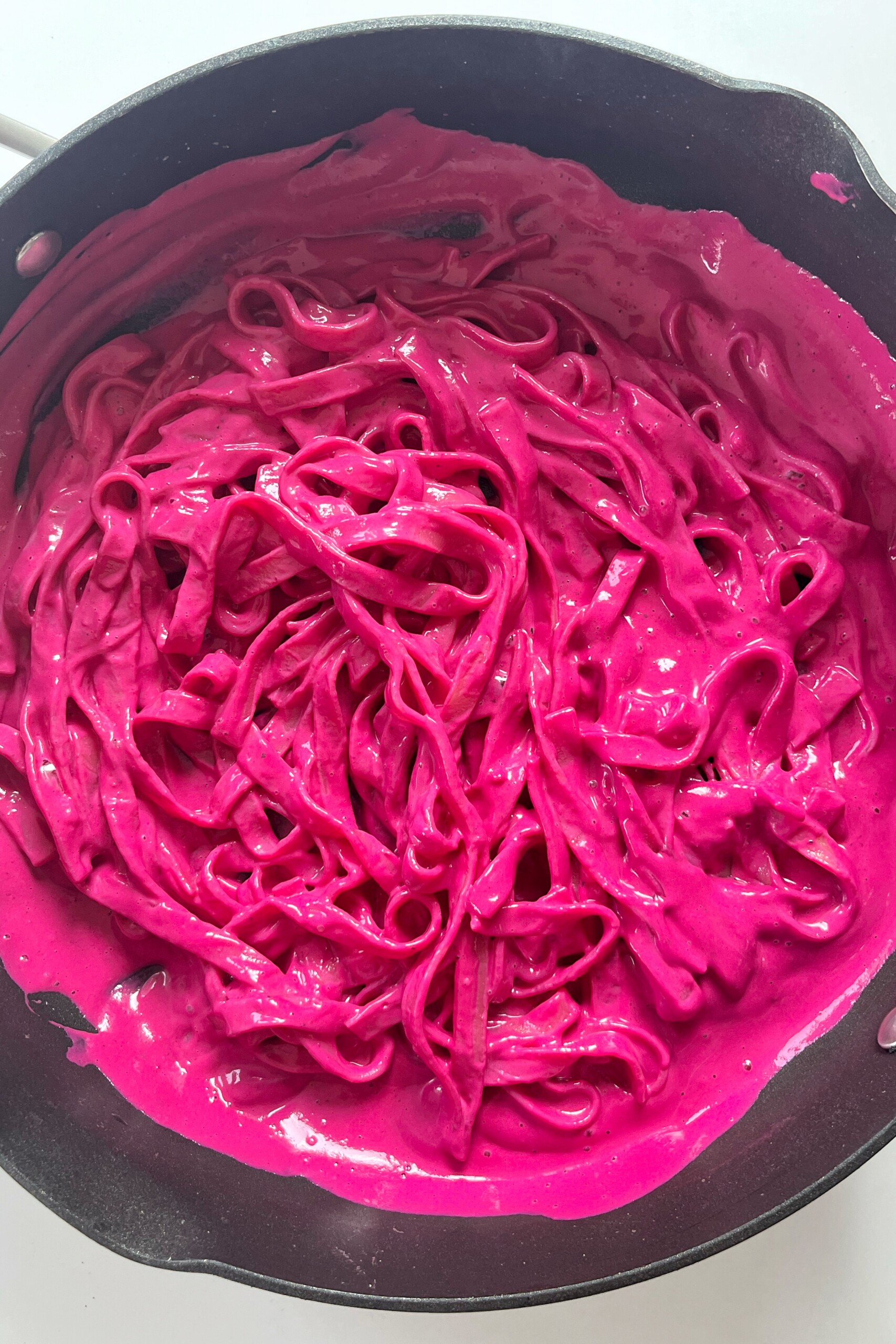 Pink pasta in a black frying pan.