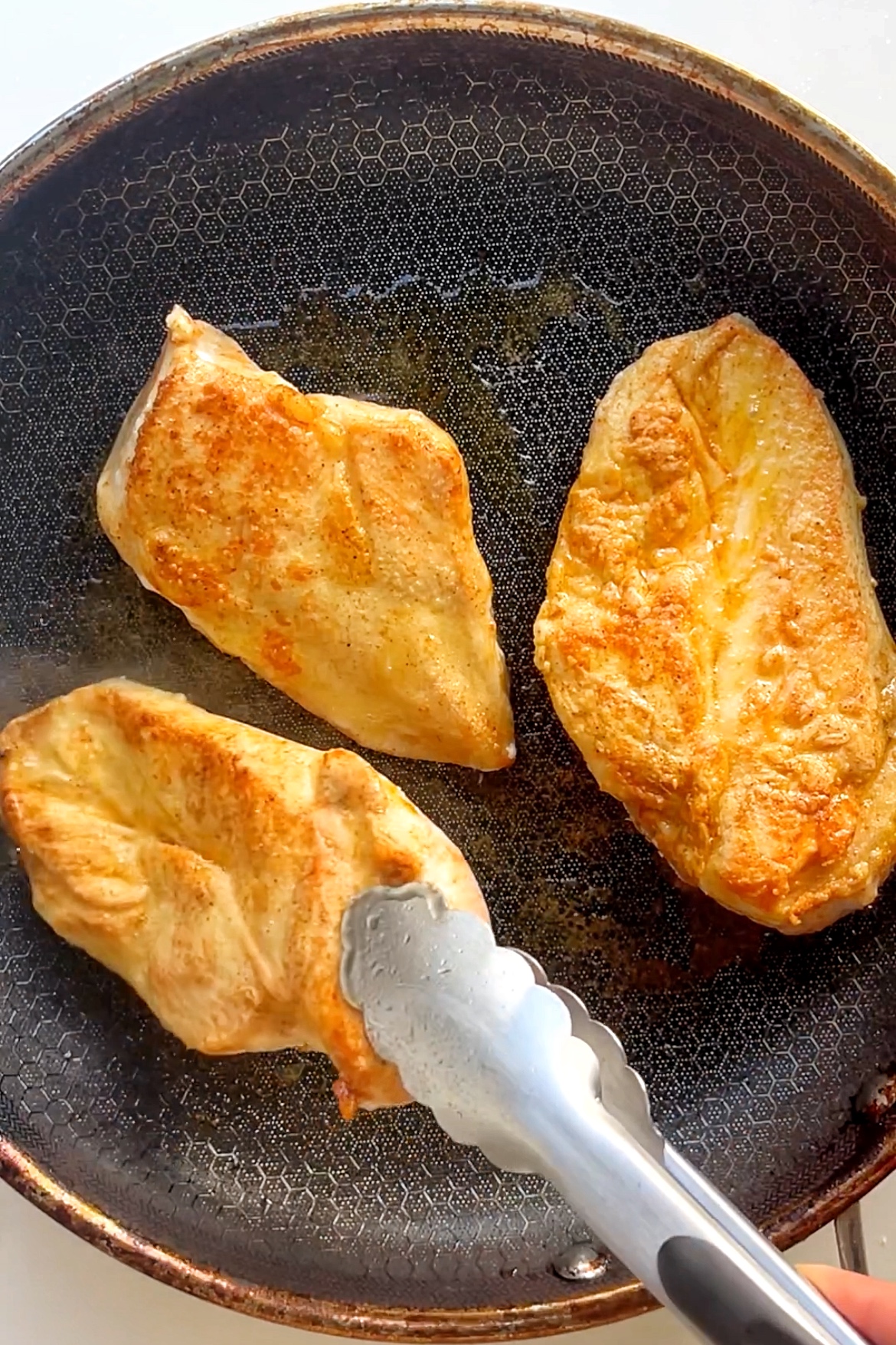 Chicken breast frying in non-stick pan.