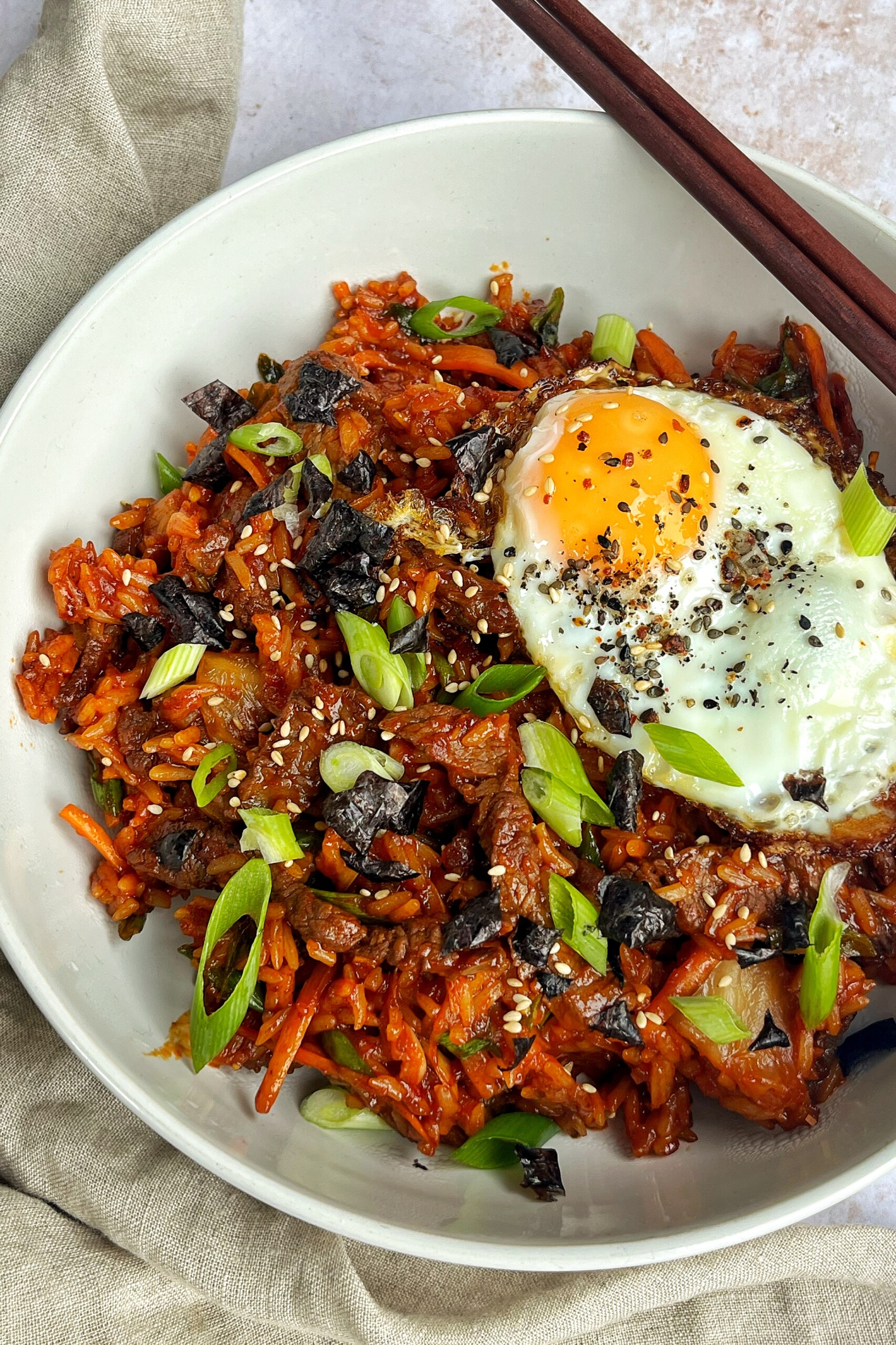 Close up of bulgogi fried rice with an egg and chopsticks in white bowl.