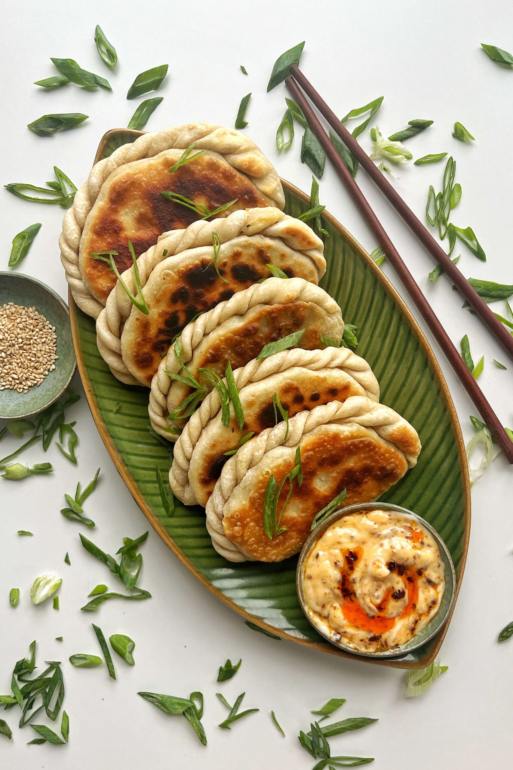 Chinese chive pockets on a green plate with chopsticks and some sesame seeds.