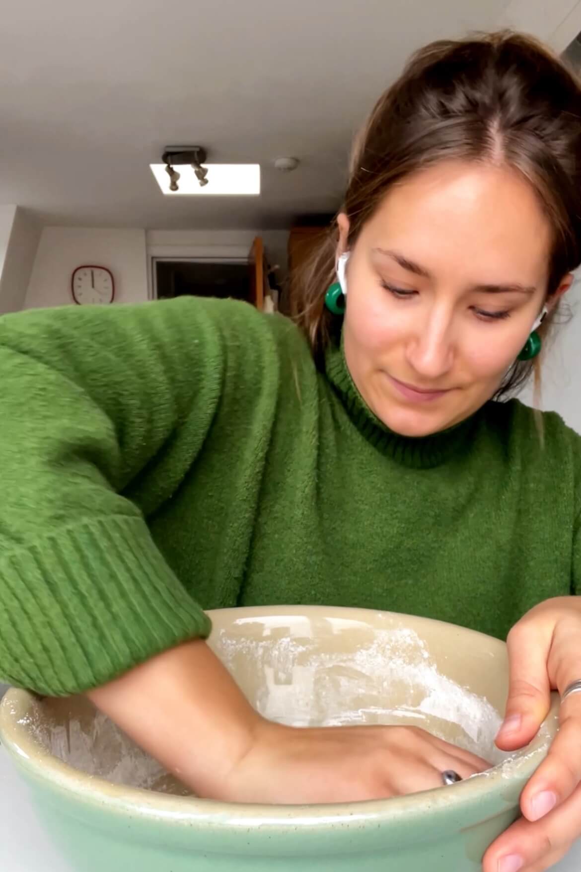 Girl kneading dough with hand in bowl.