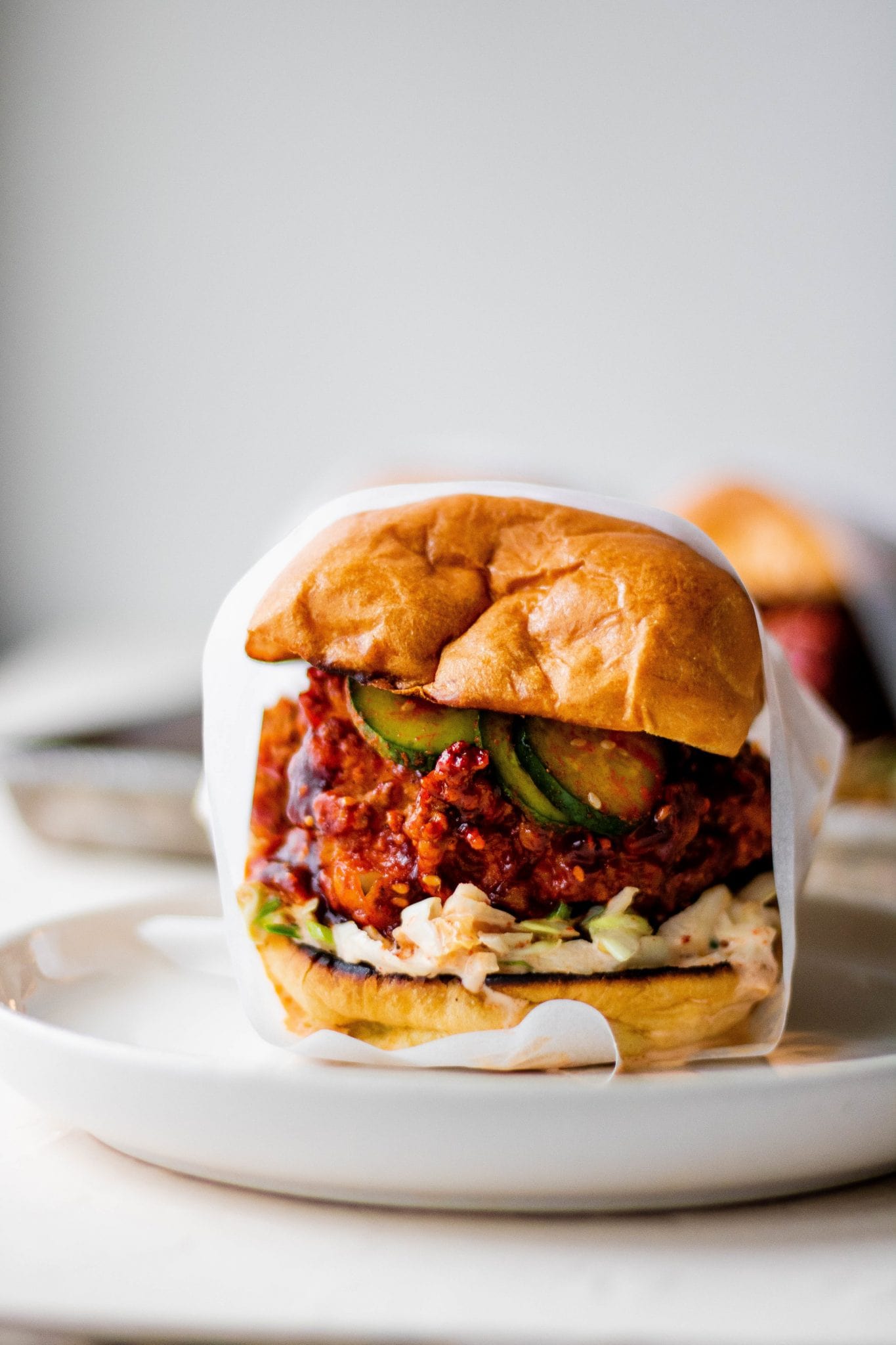 Gochujang chicken sandwich on a white plate wrapped in parchment paper.