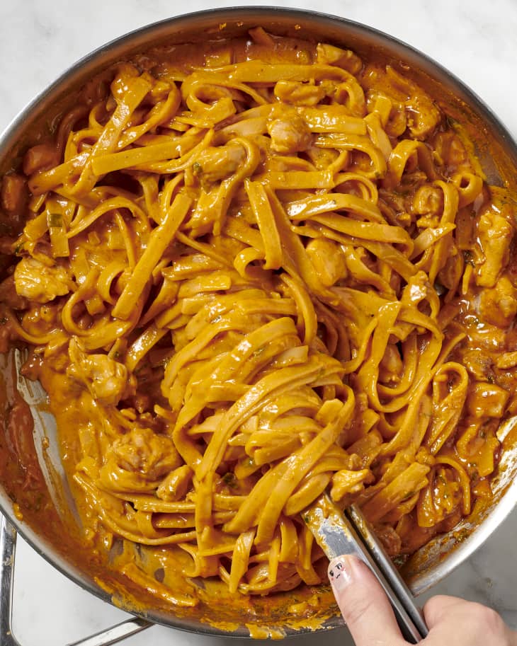 Saucy gochujang chicken pasta with tongs.