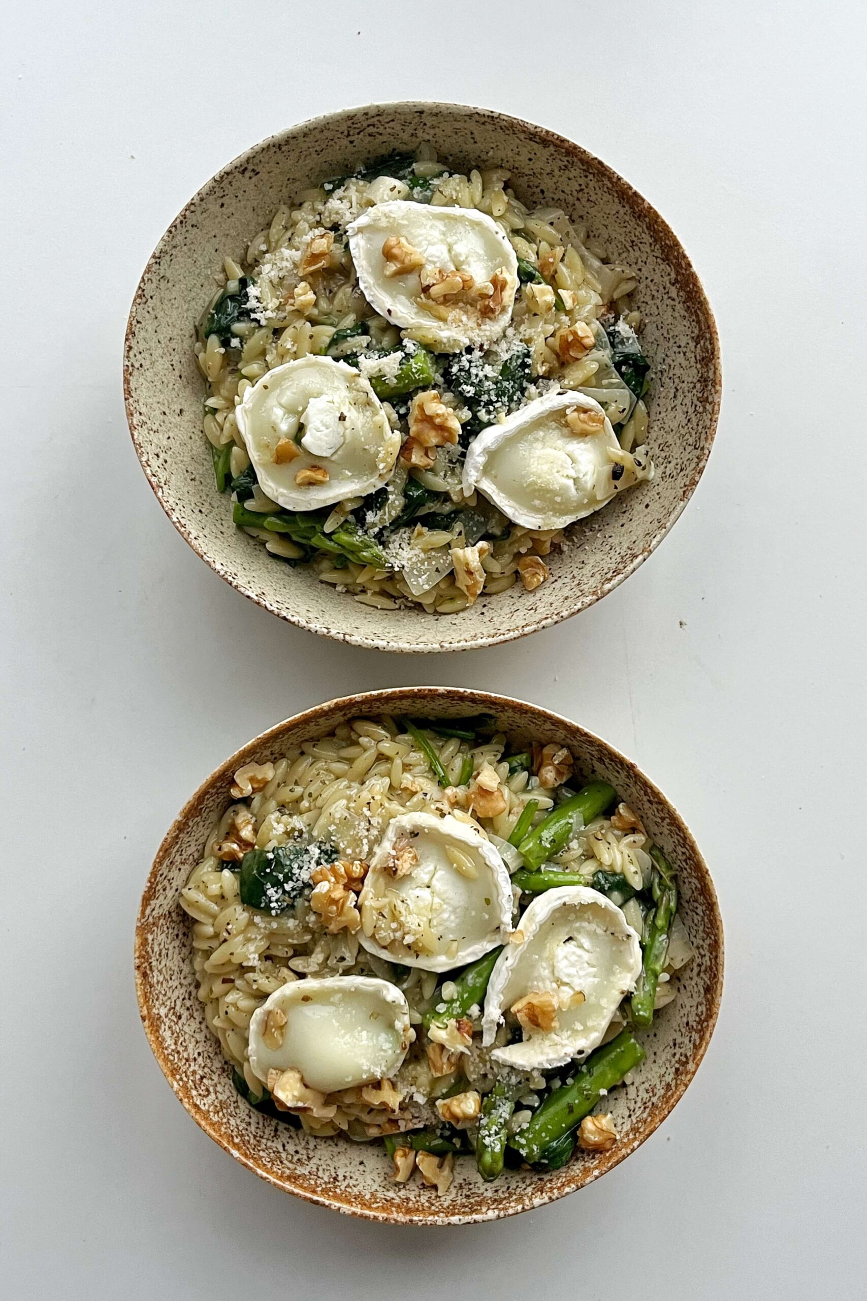 Two bowls of asparagus orzotto topped with goats cheese.