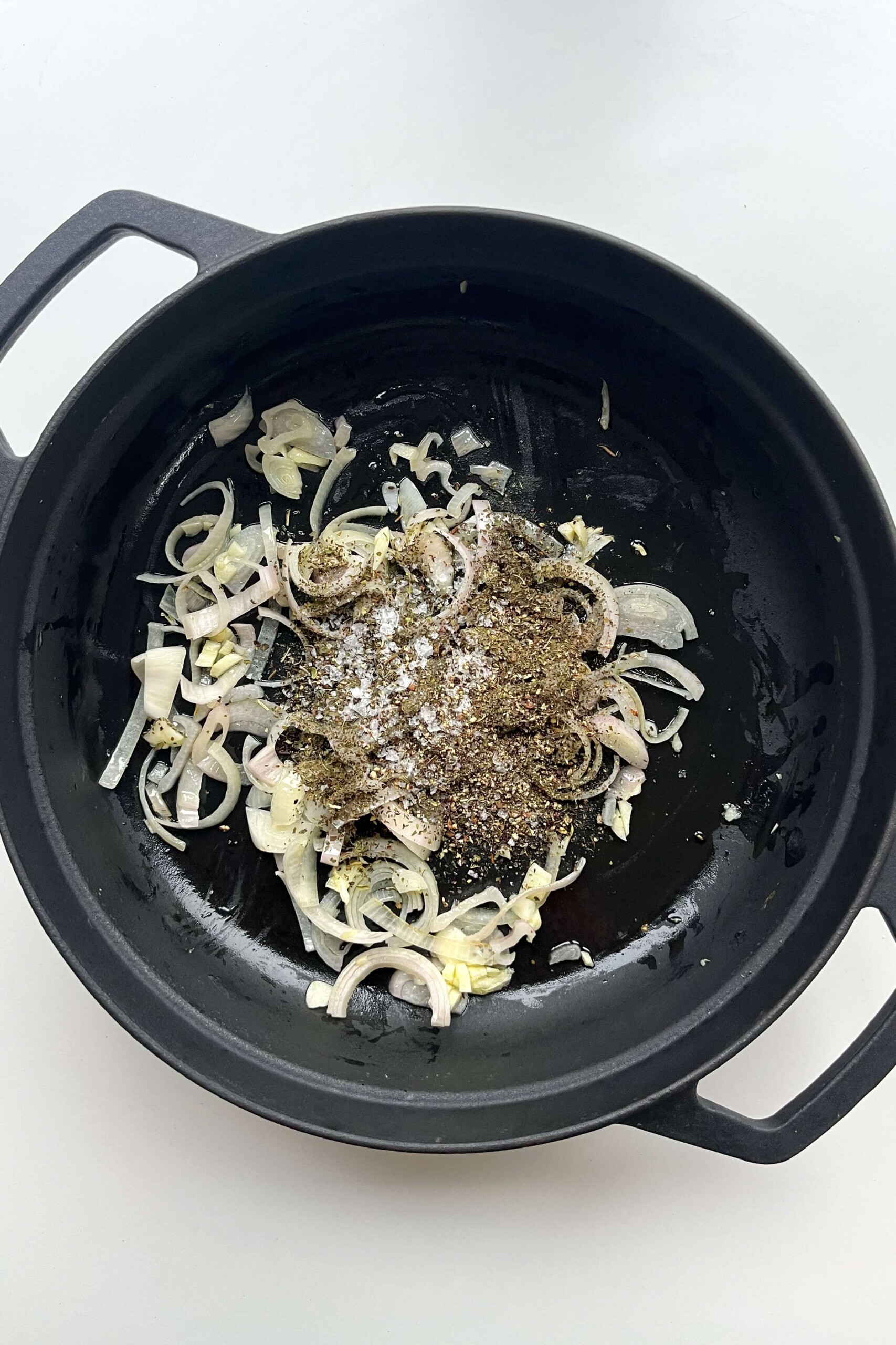 Frying shallots, herbs, garlic in a black pan.