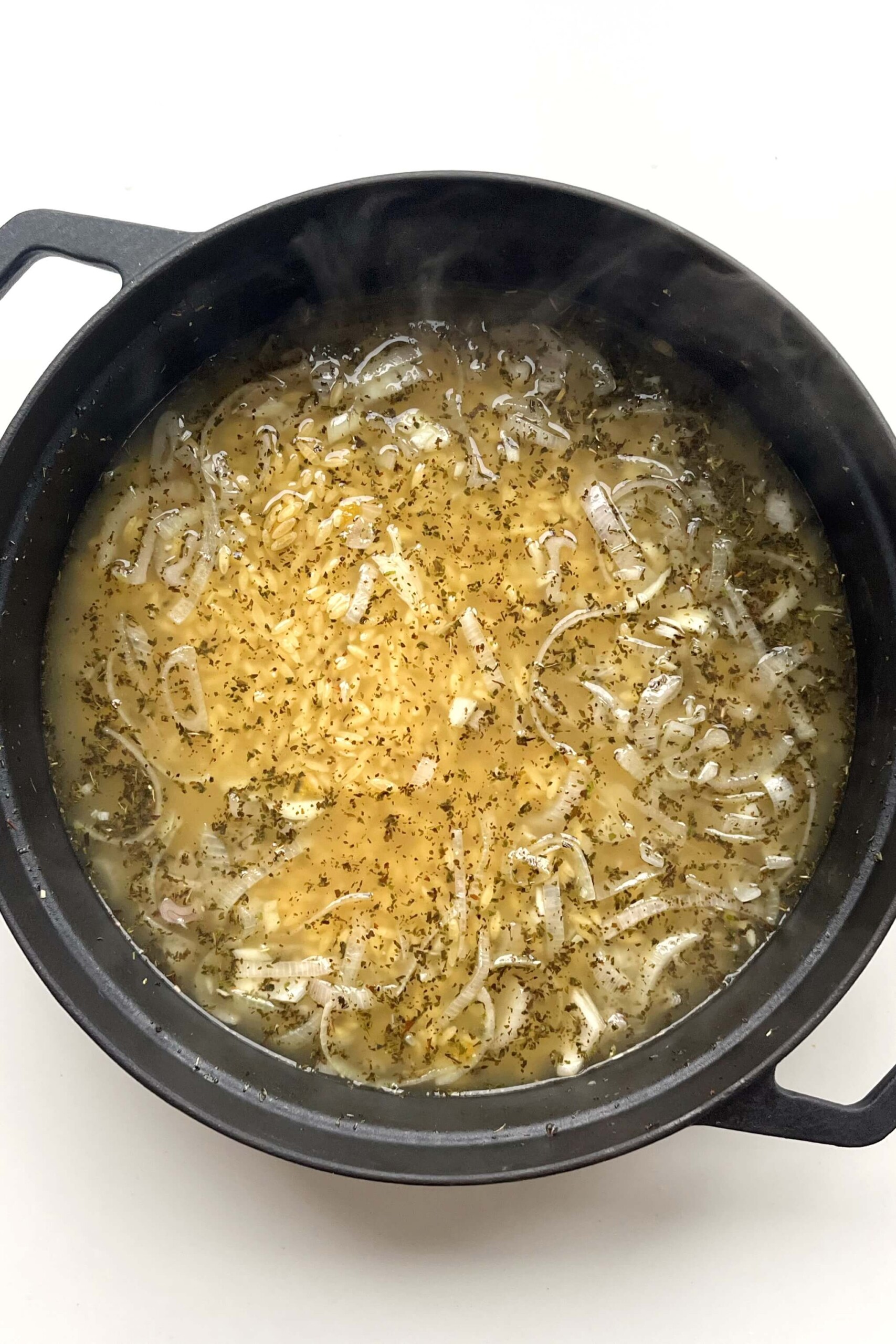 Black pan with orzo and stock inside.