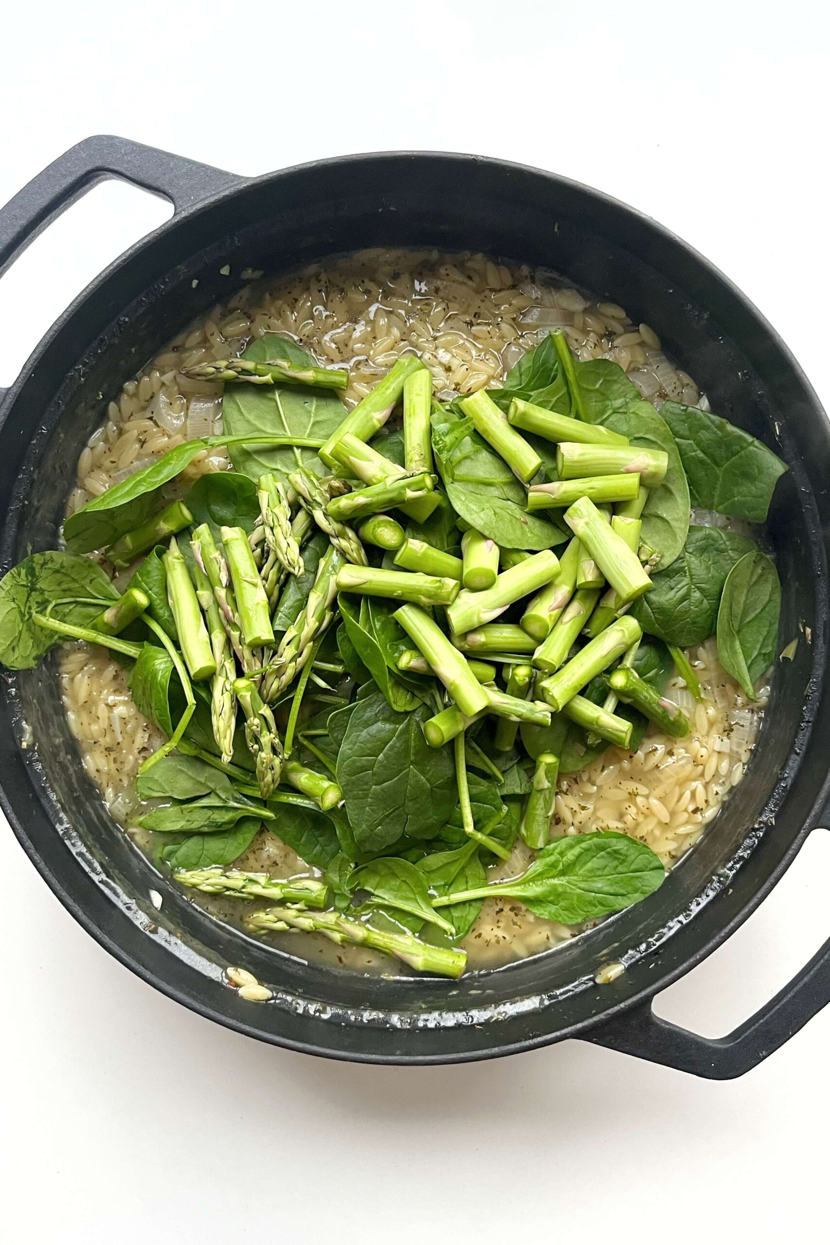 Black pan with orzo, stock, spinach, and asparagus.