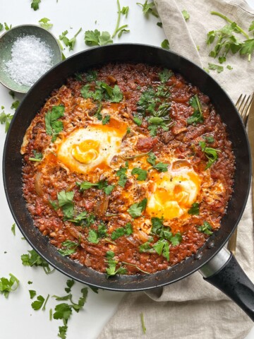 Sardines and eggs in a black pan with sprinkled parsley.