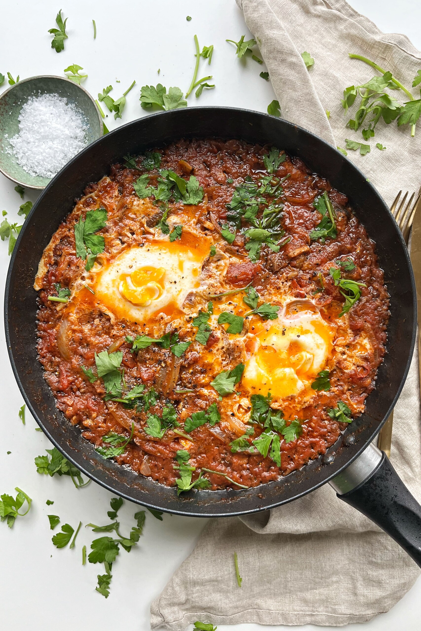 Sardines and eggs in a black pan with sprinkled parsley.