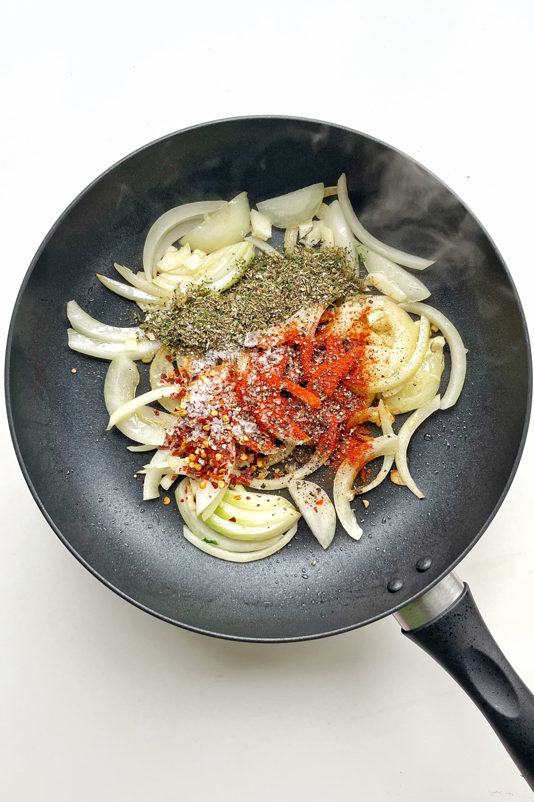 Black pan with fried onions, garlic, herbs, and spices.