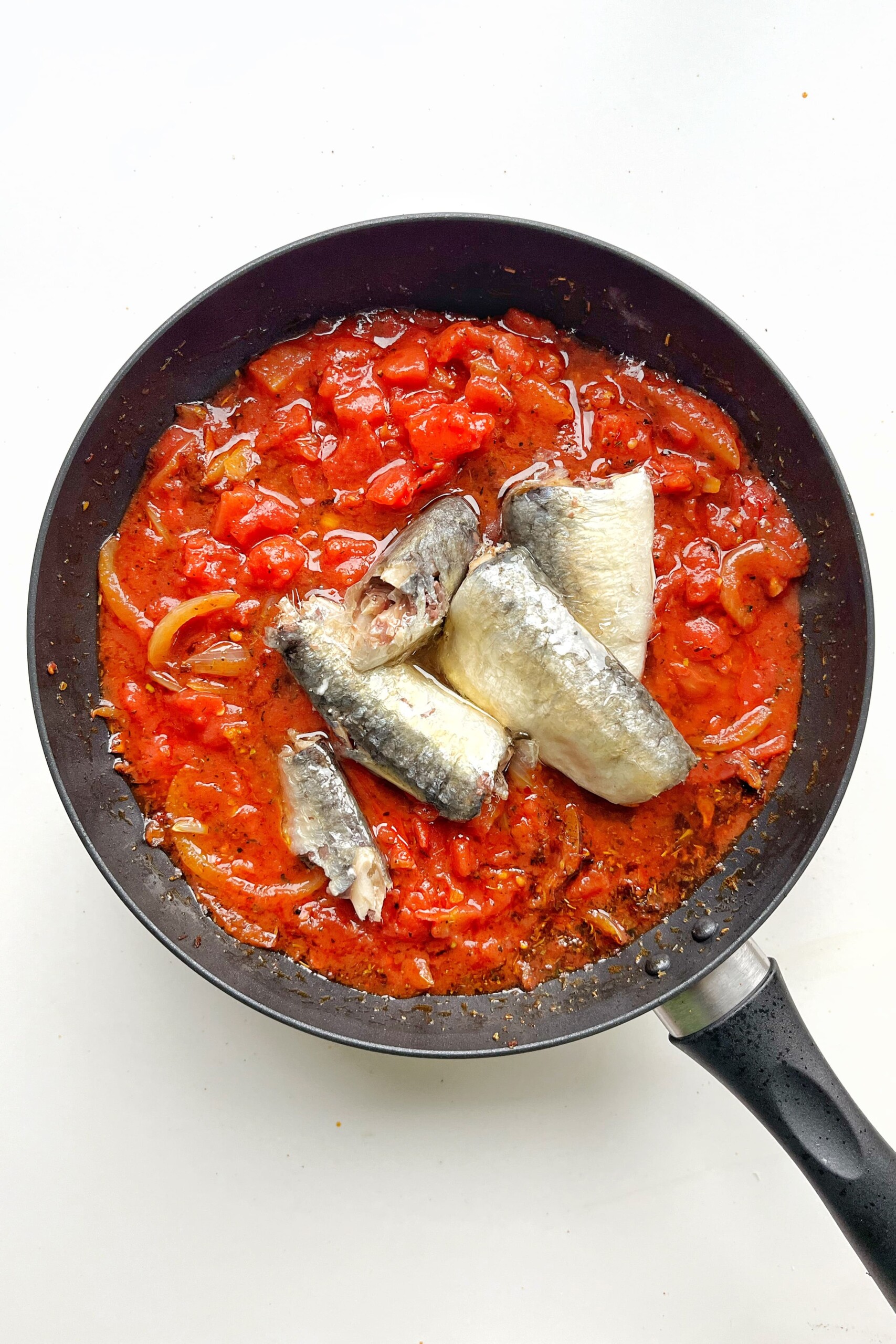 Black pan with tomatoes, sardines, and spices in it.
