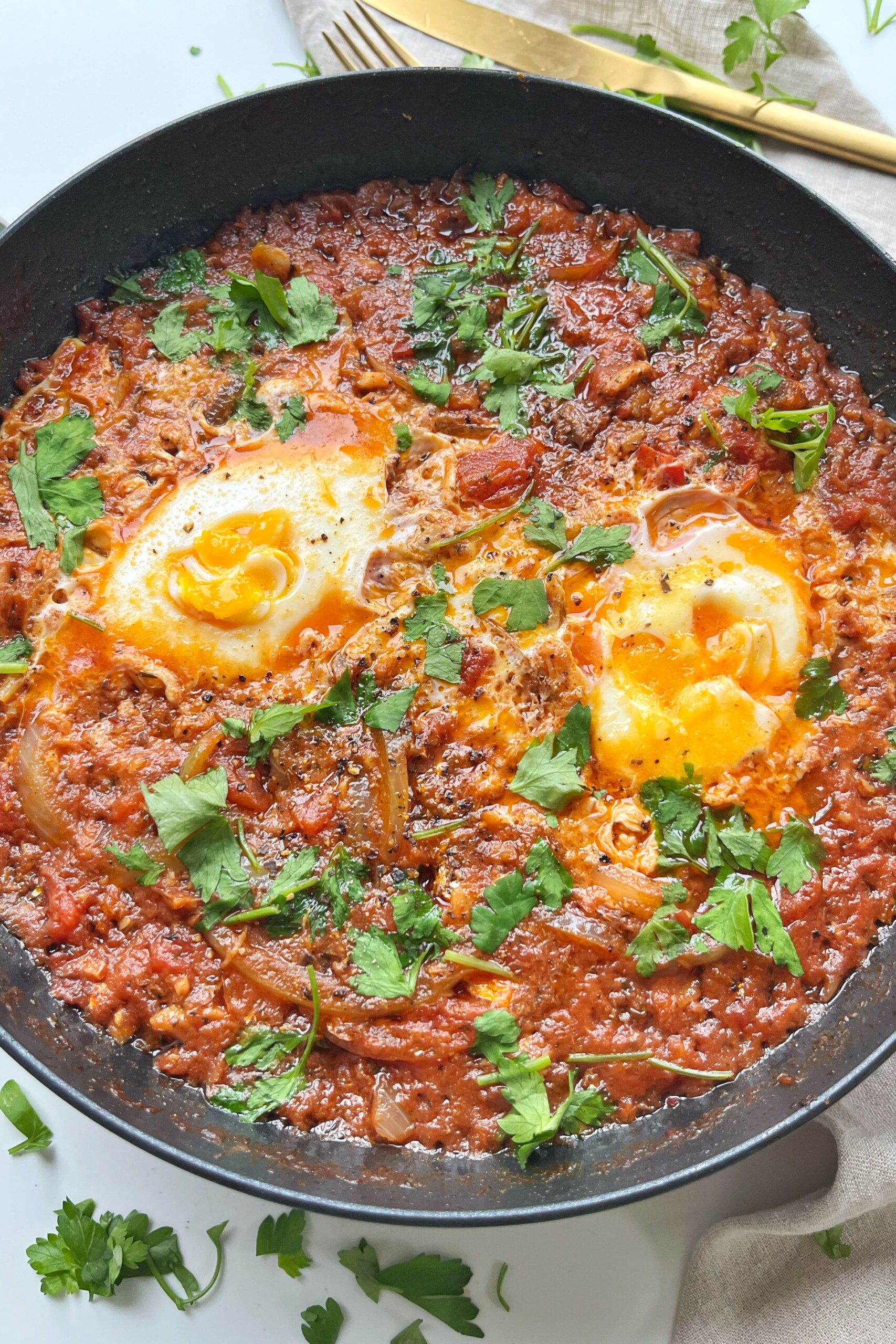 Close up of sardines and eggs in a black pan with a sprinkle of parsley.