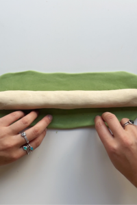 White dough sausage placed on top of a green rectangle of dough.