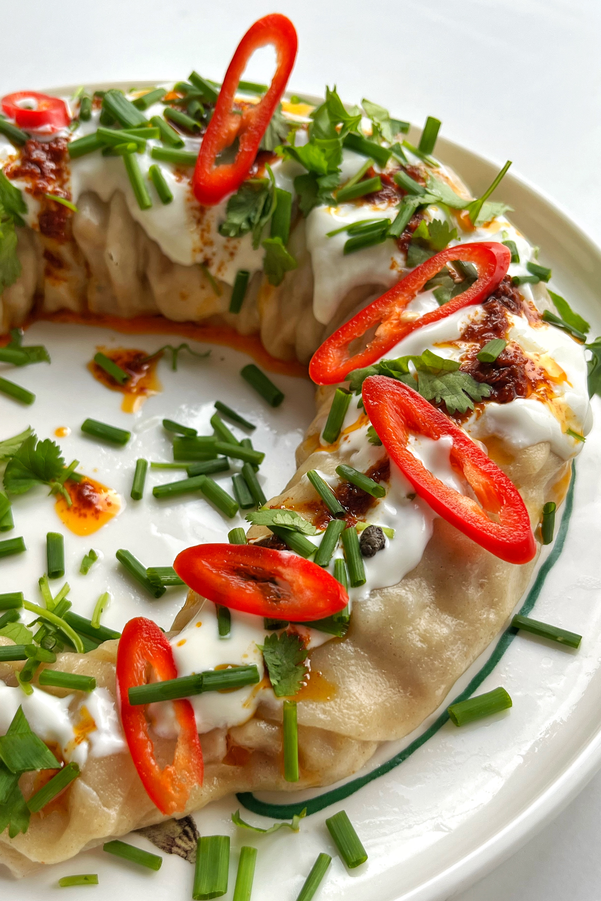Close up of the dumpling wreath topped with coriander, chives, yoghurt, and red chillies.