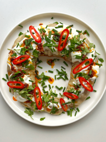 Dumpling wreath on a white plate topped with yoghurt, harissa oil, chives, and sliced chilli.