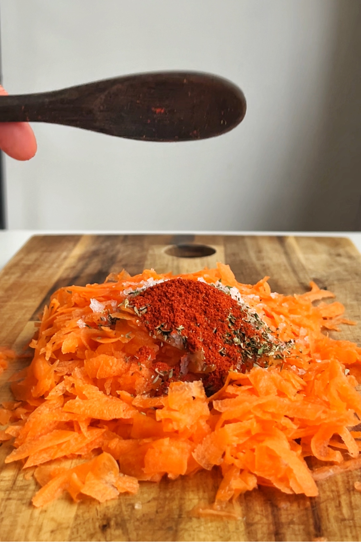 Pouring herbs and spices onto grated carrot with black wooden spoon.