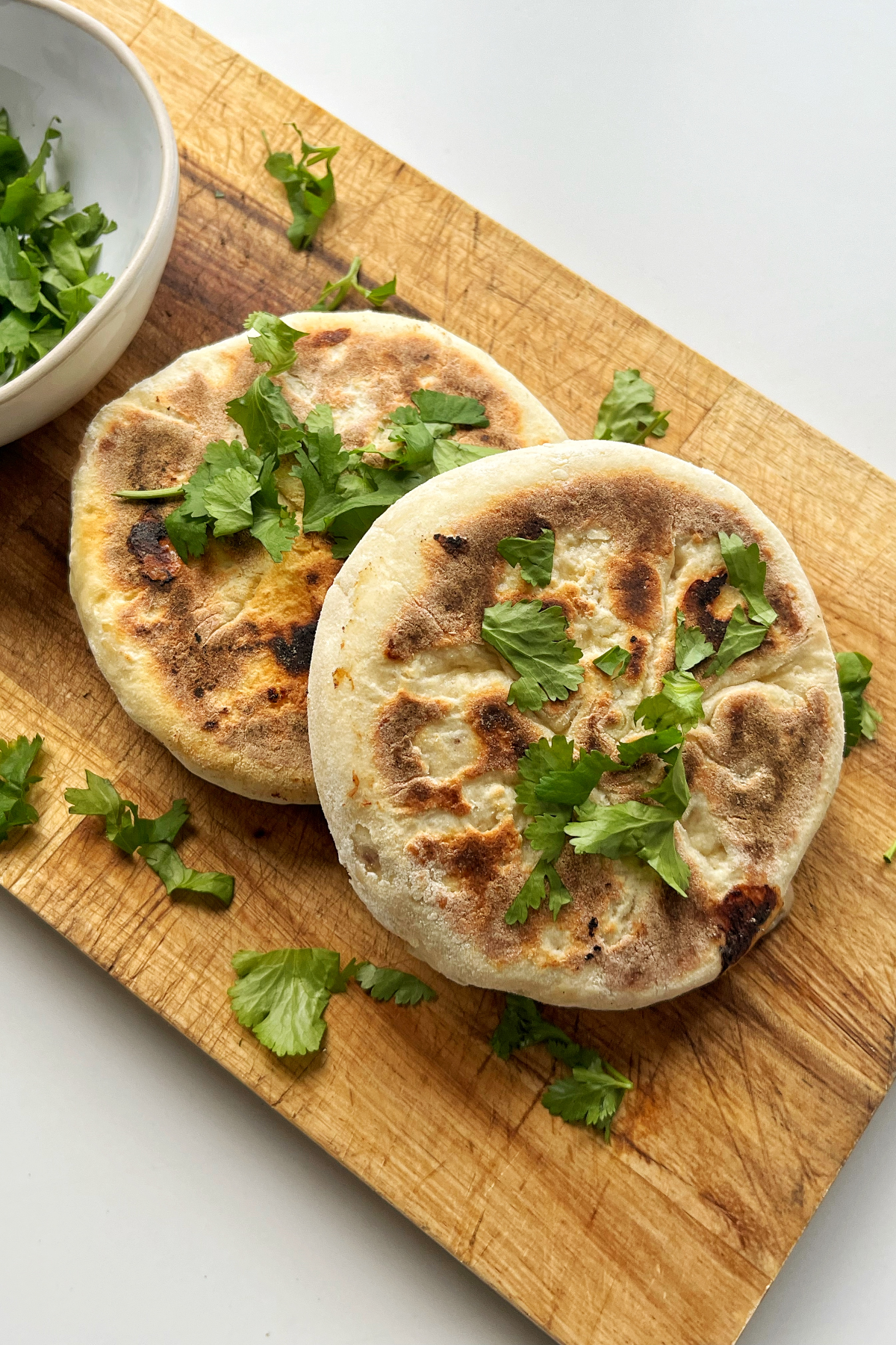 Flatbreads topped with parsley and on a brown wooden board.