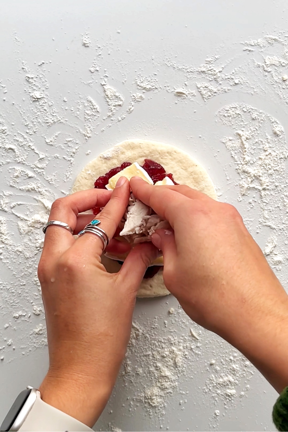 Wrapper of dough that is being filled with cranberry sauce, turkey, and brie.