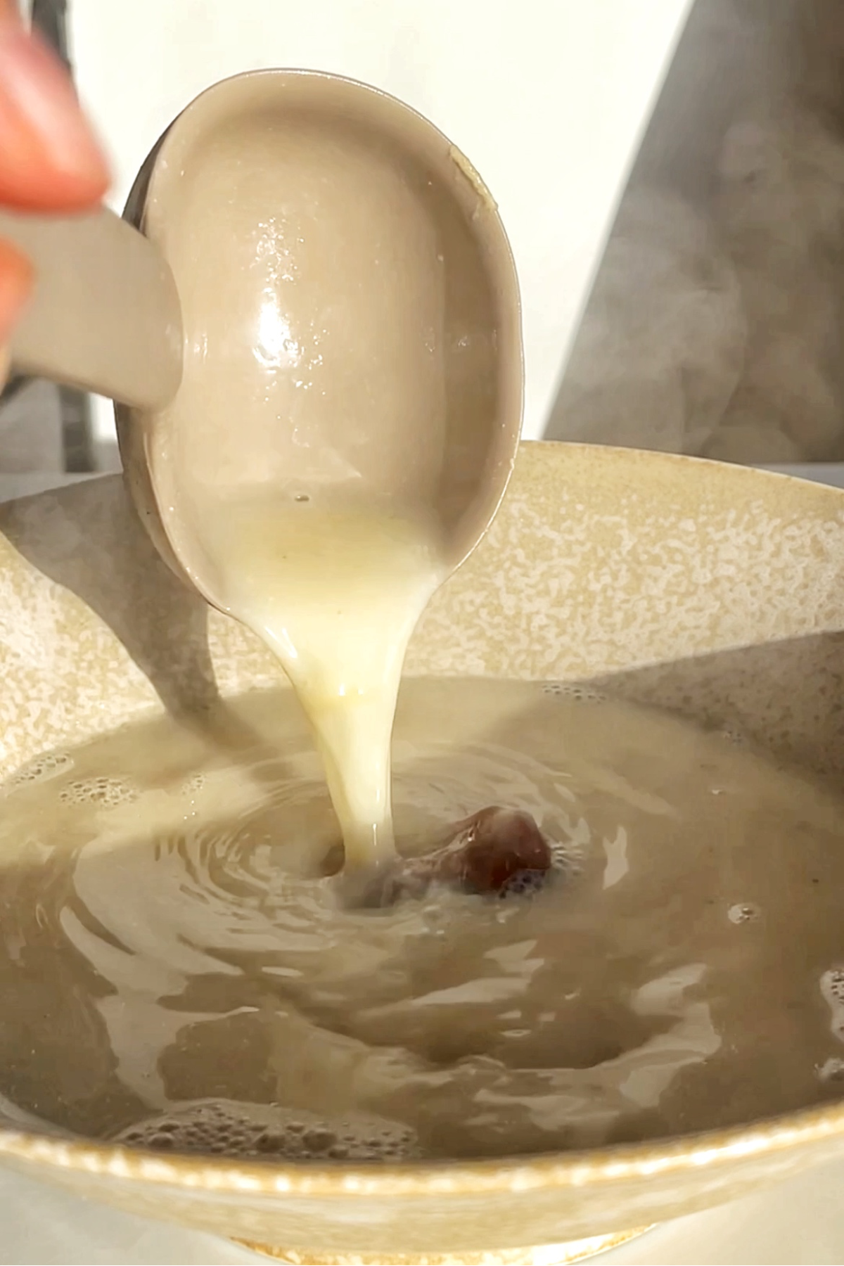 Pouring turkey broth into a ramen bowl using a ladle.