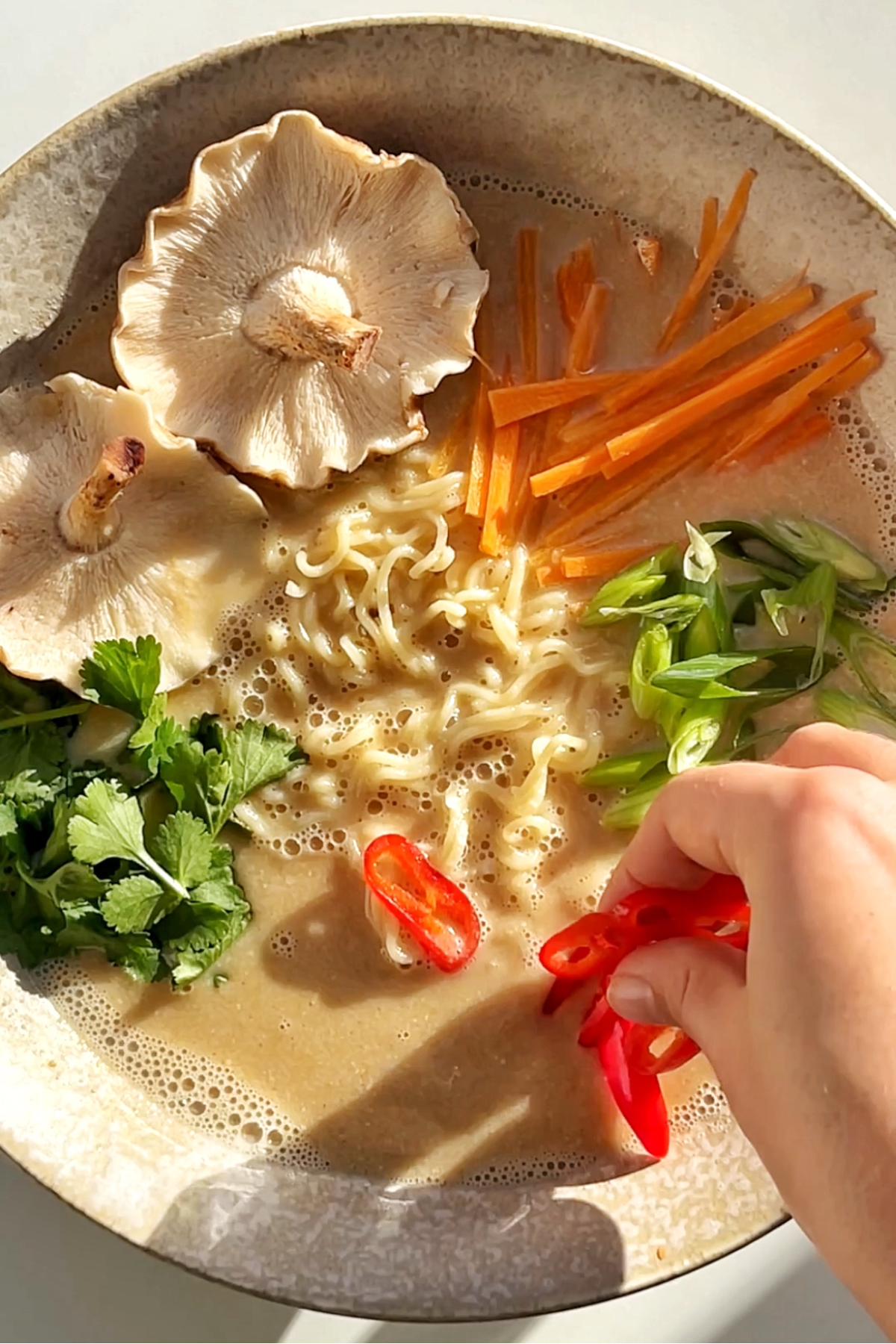 Placing garnishes on top of a ramen bowl.