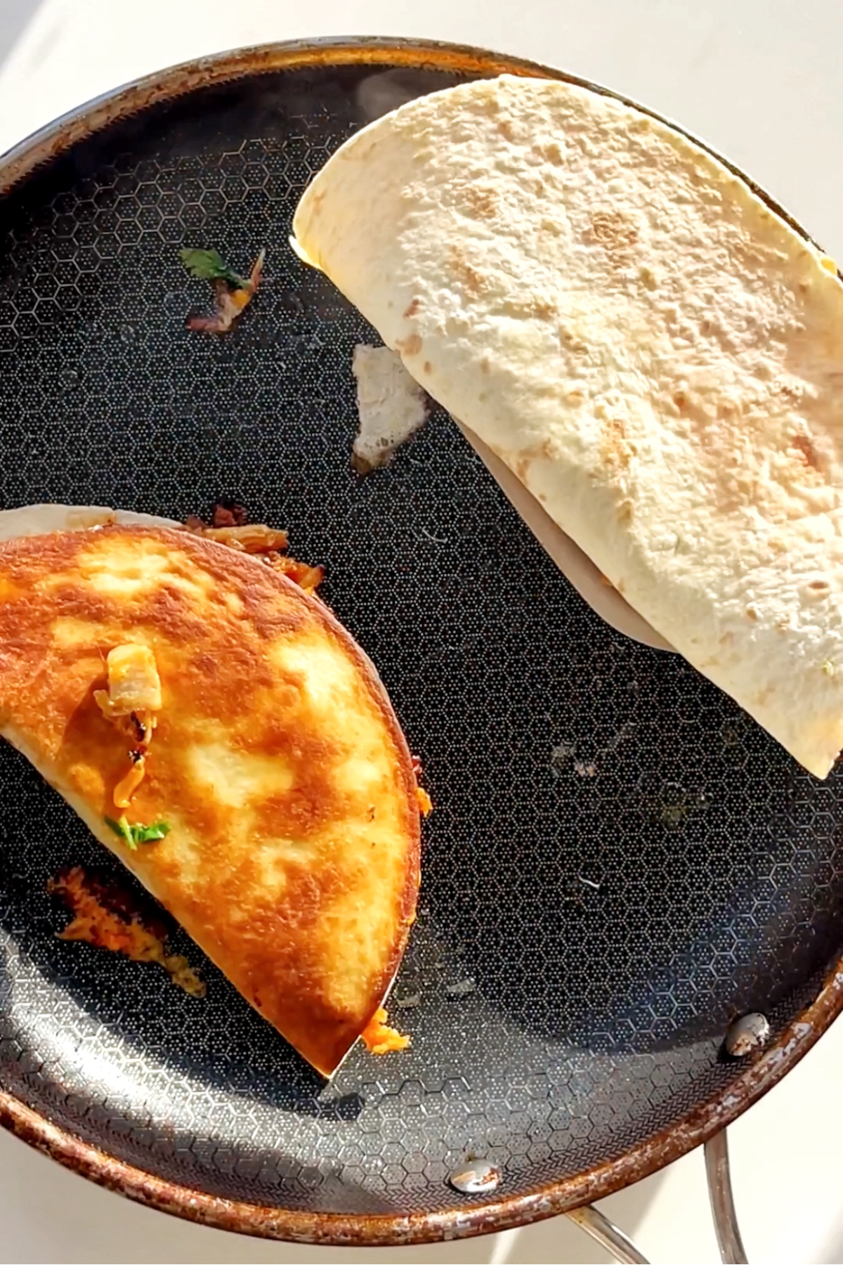 Black pan with half moon shaped quesadillas being fried.