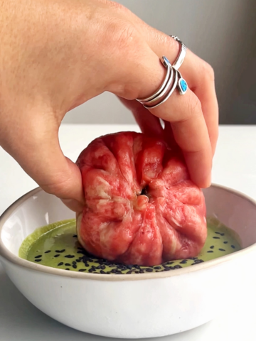 Dipping the grinch dumplings into a green tahini sauce in white bowl.