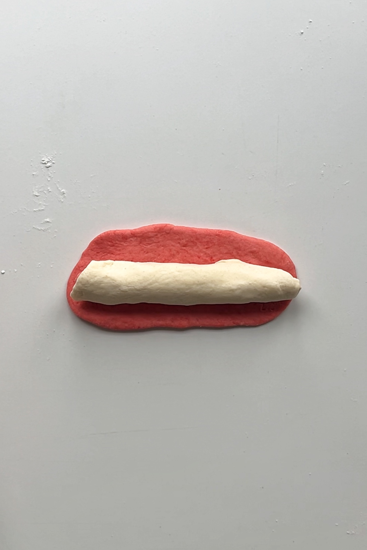 Placing white roll of dough onto pink sheet of dough.