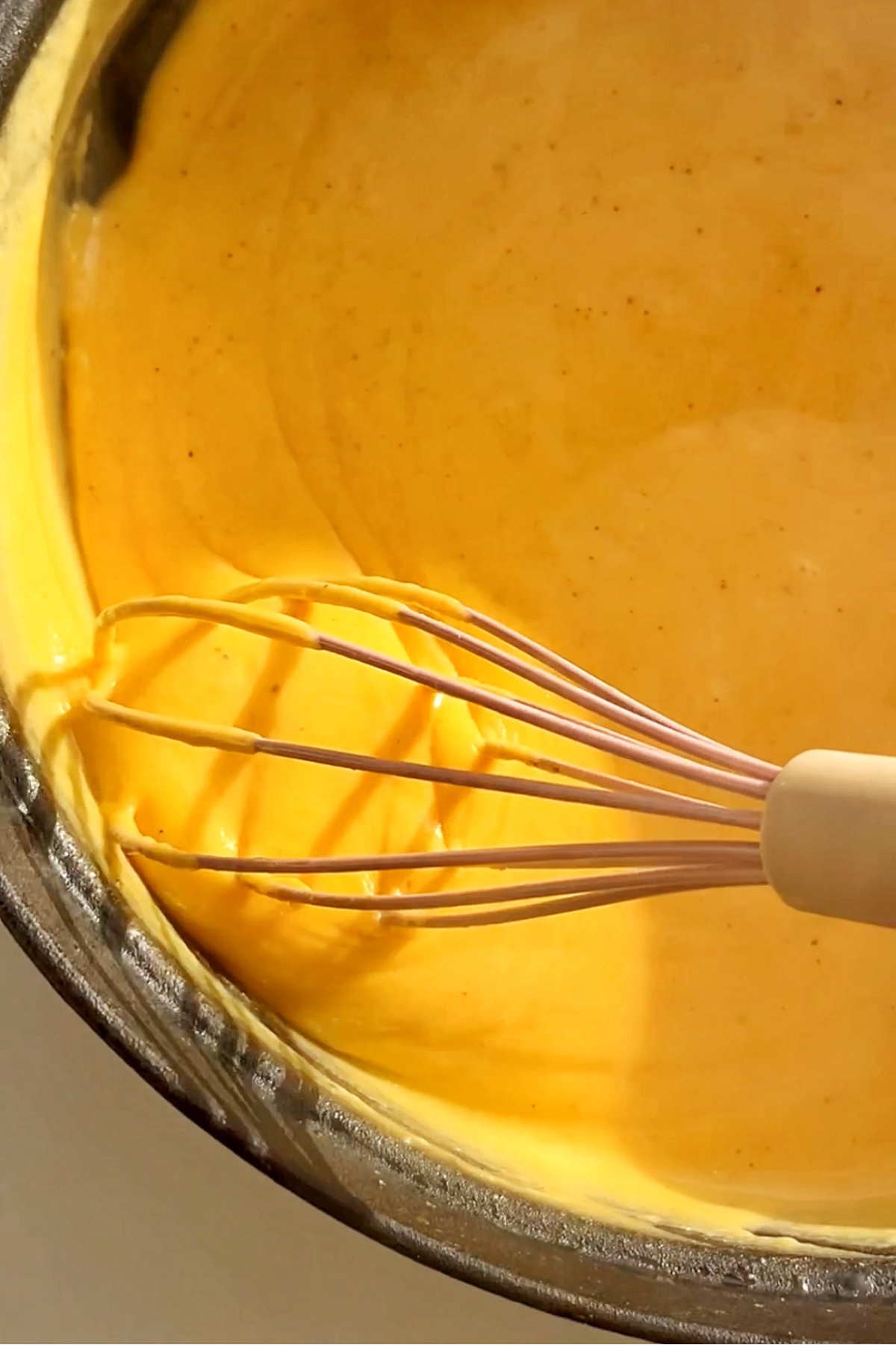 Stirring a whisk in a yellow cheese sauce.
