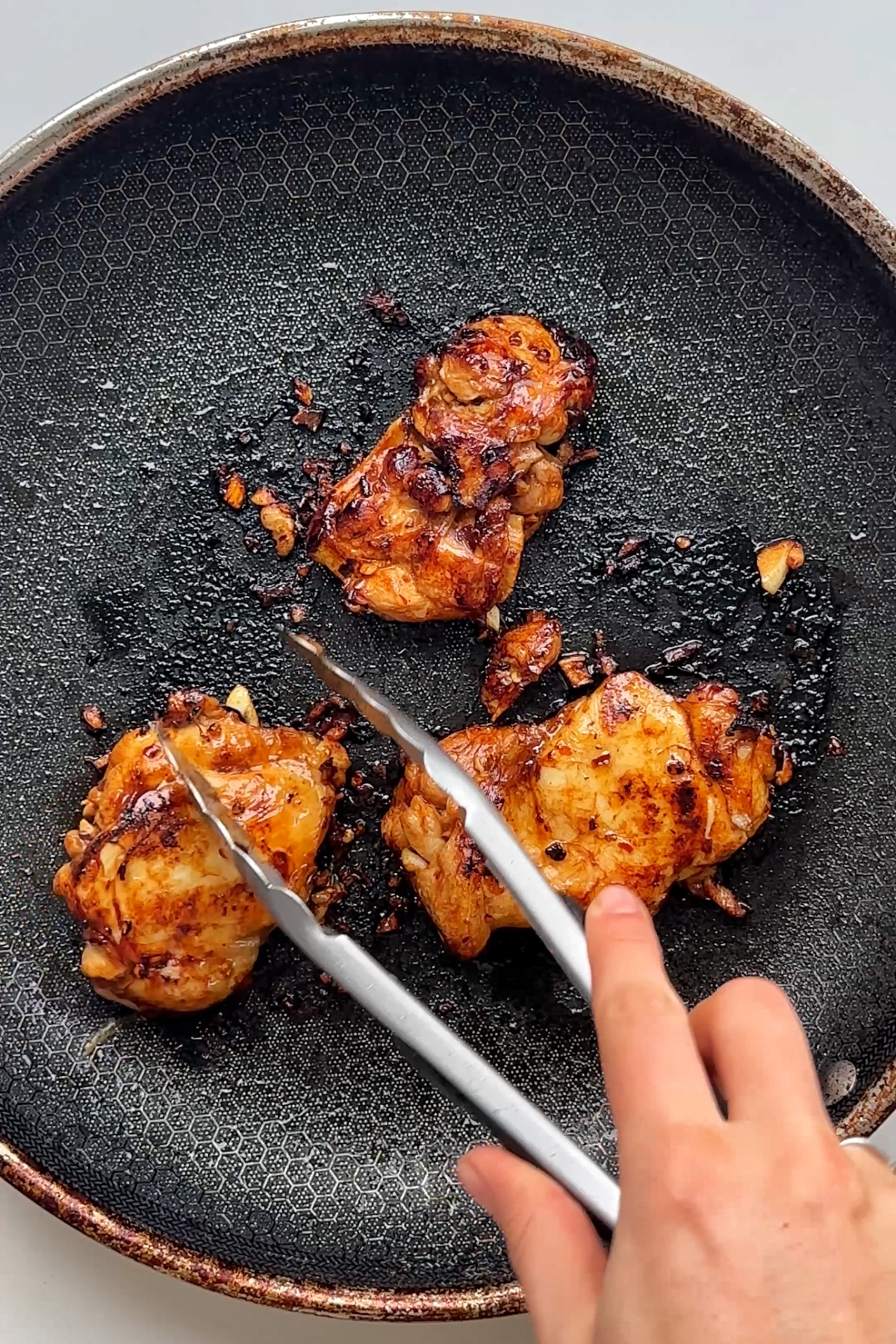 Frying chicken thighs in black pan.