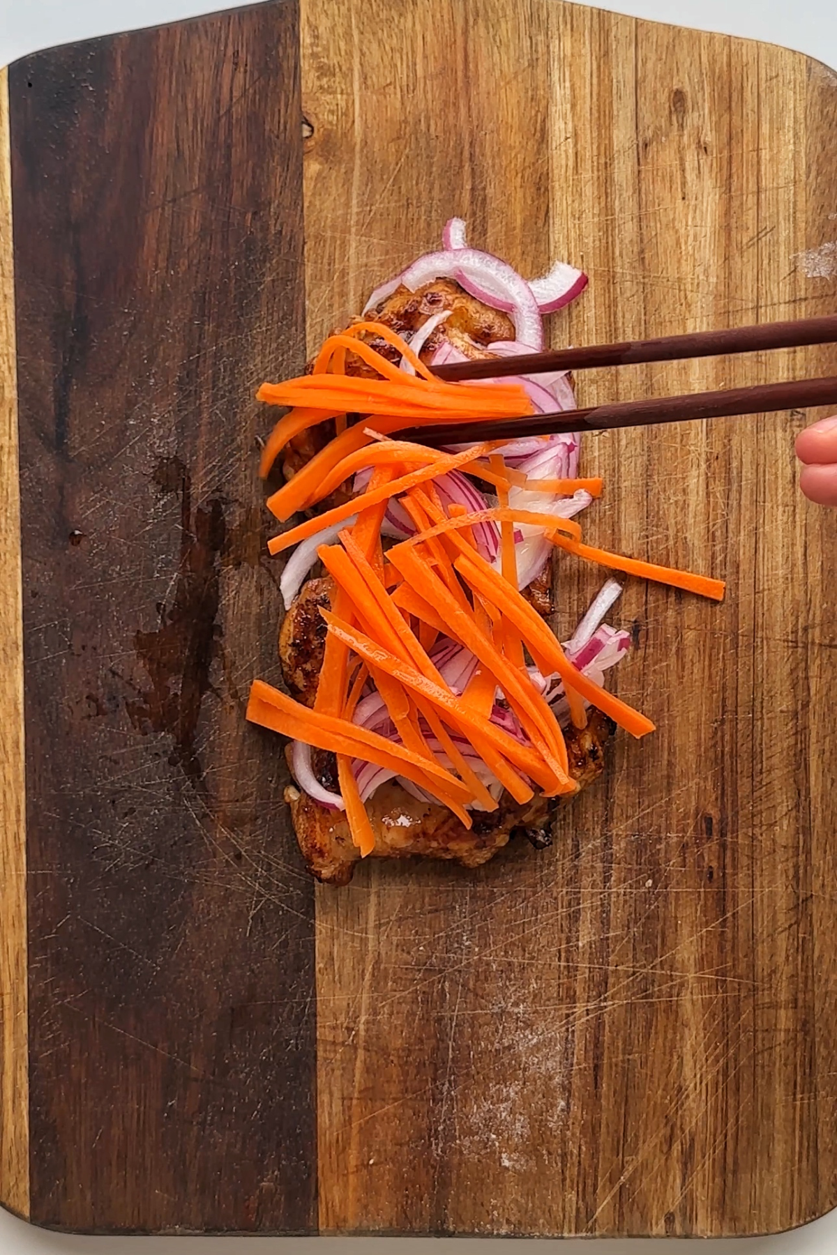 Adding ingredients onto a chopping board with chopsticks.