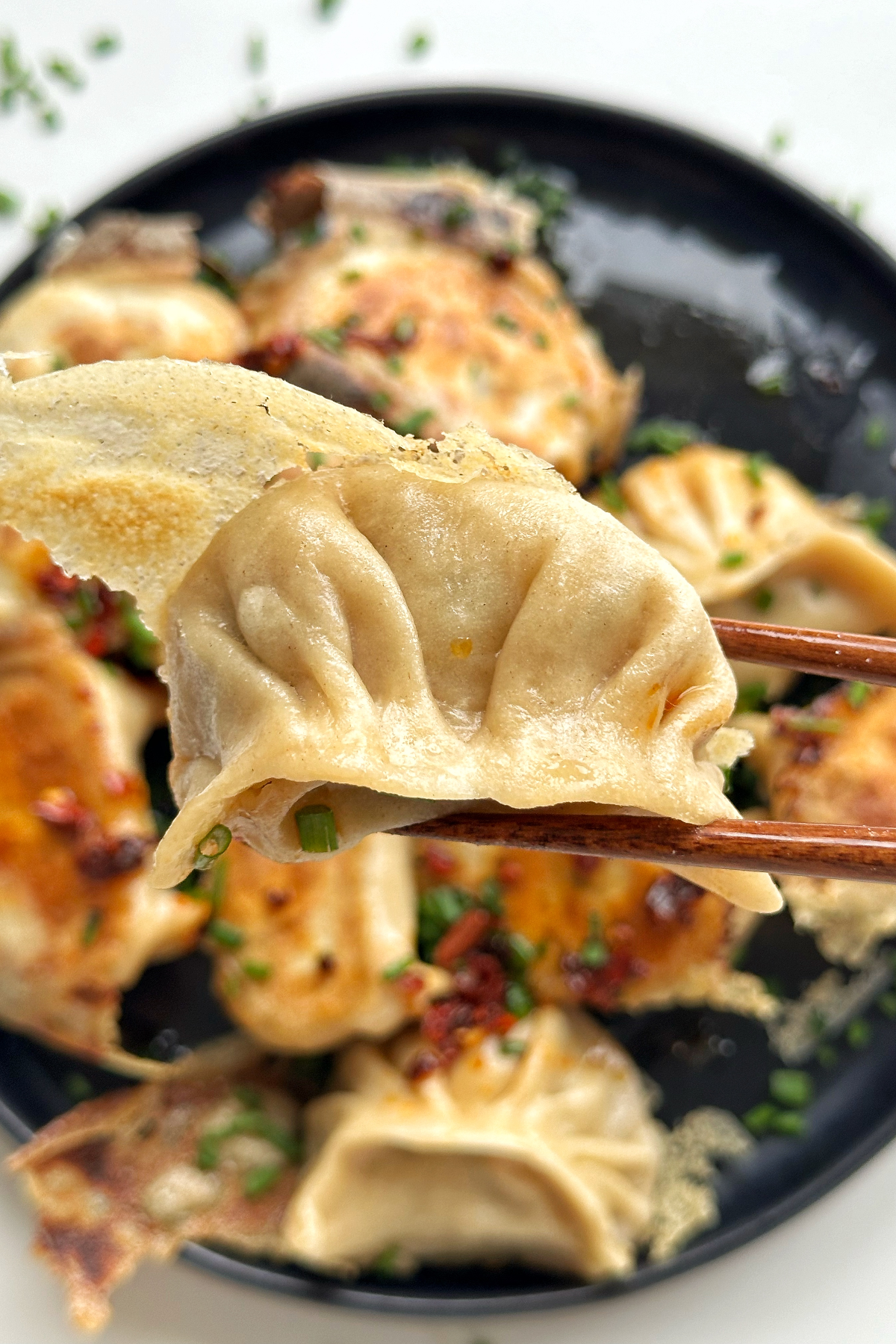 Close up of a dumpling held by chopsticks on a black plate.
