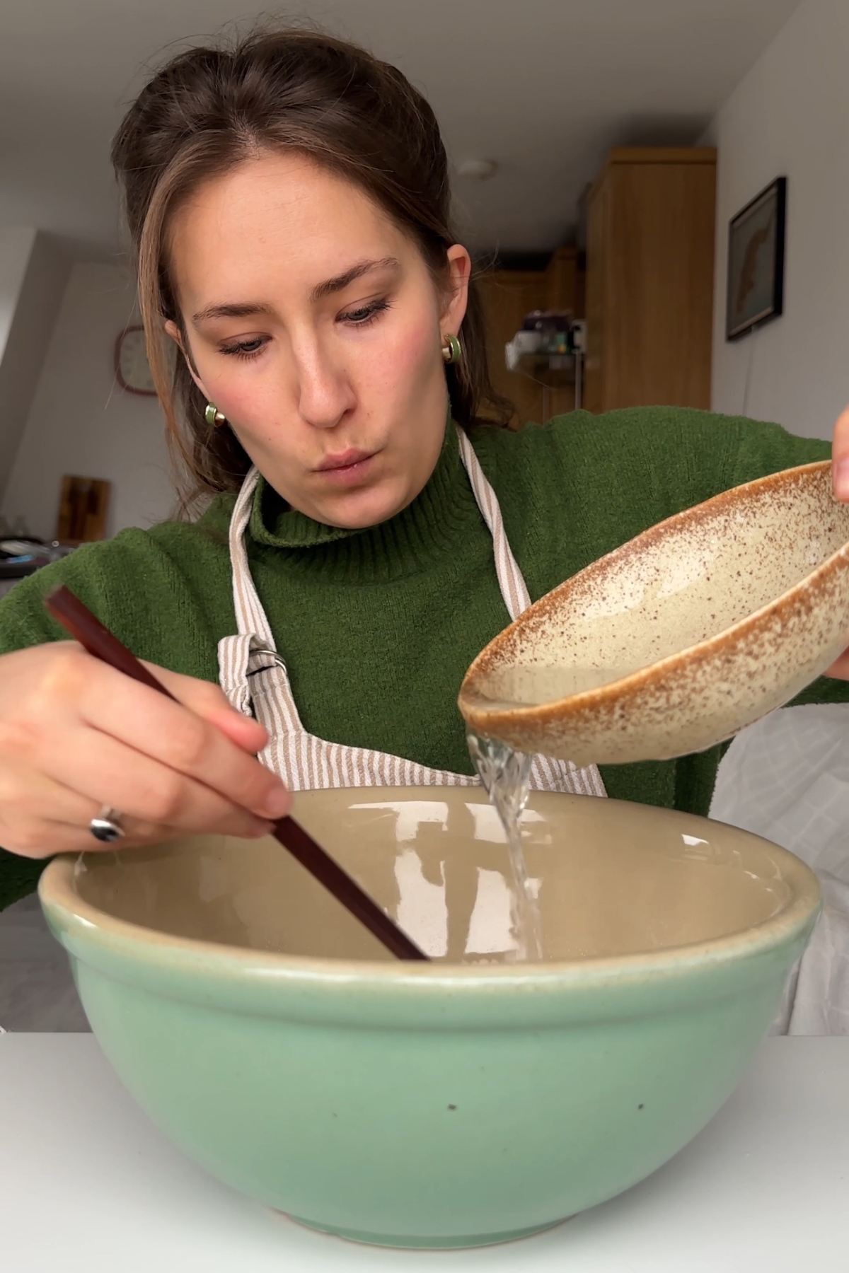 Emily Roz pouring water into a blue bowl with chopsticks in her right hand.
