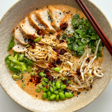 Marry me chicken ramen in a ramen bowl with chopsticks topped with chicken, edamame beans, coriander, beansprouts, and spring onions.