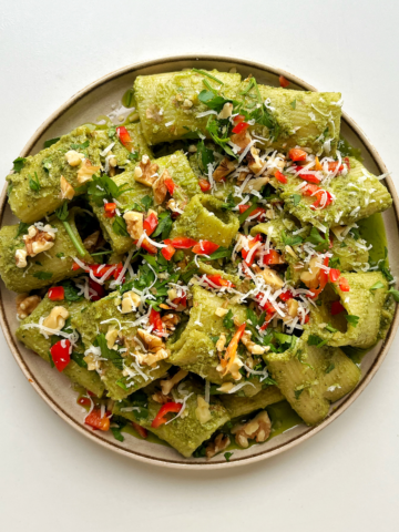 Zhoug-inspired rigatoni with walnuts, parsley, and chilli on a cream plate with a white background.
