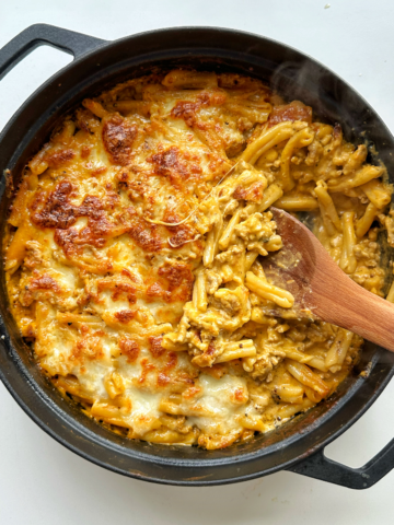 Black oven proof dish filled with baked pasta with a wooden spoon off the side.