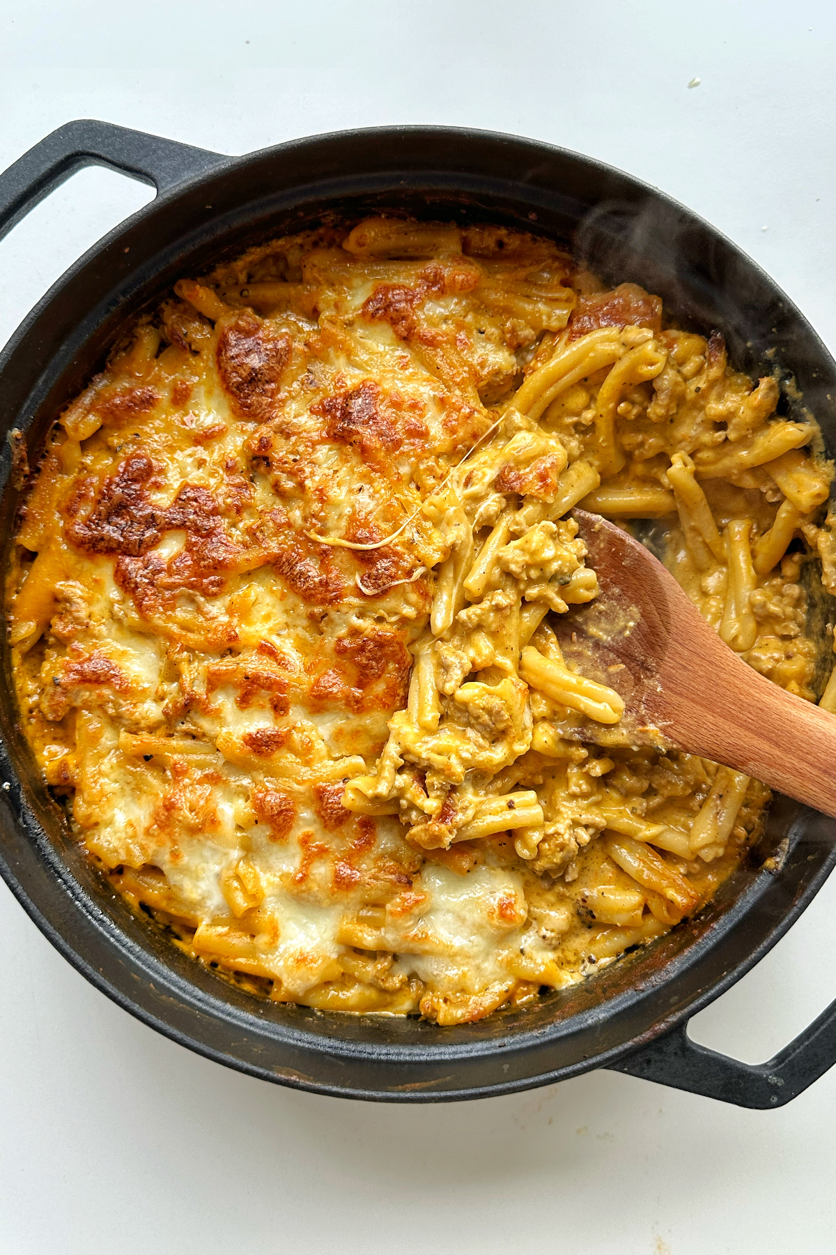 Black oven proof dish filled with baked pasta with a wooden spoon off the side.