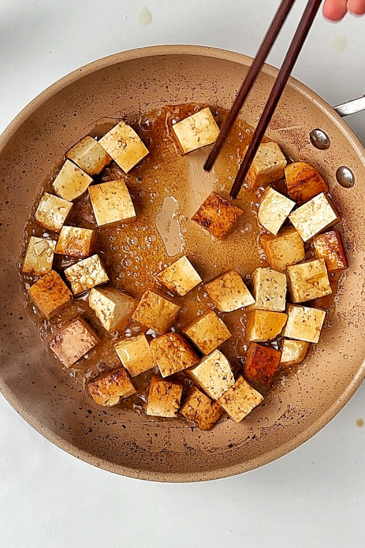 Frying cubed tofu in caramel pan with chopsticks.