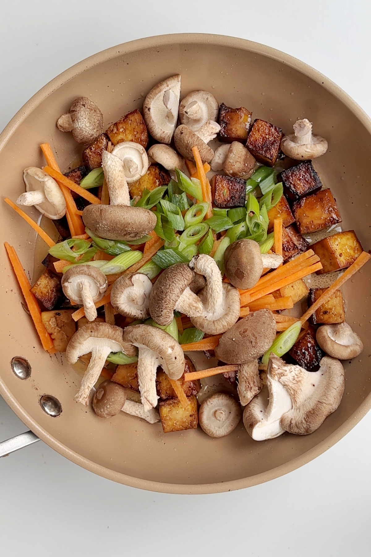 Frying veggies and tofu in a caramel pan.