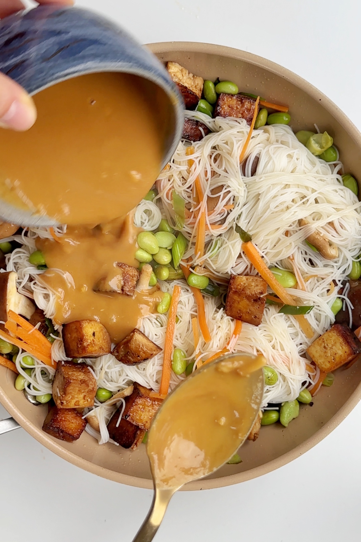 Pouring sauce into a pan with vermicelli noodles and veggies.