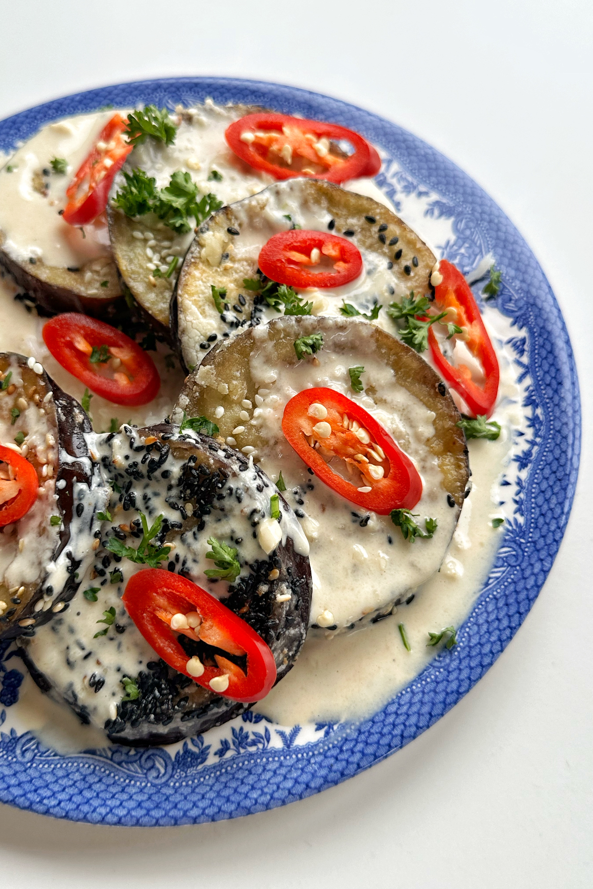Side close up of a blue plate topped with aubergine, red chillies, and chopped parsley.