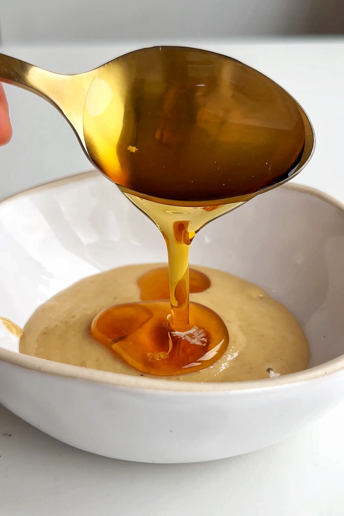 Making maple tahini sauce in a white bowl.