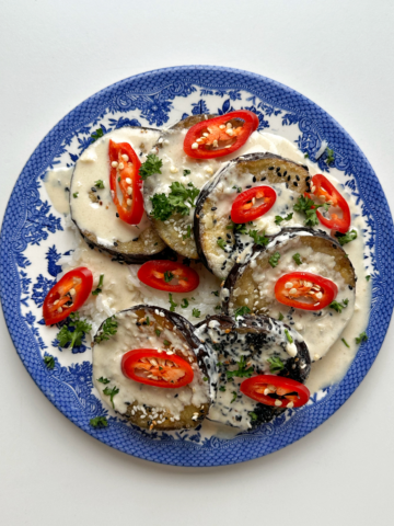 A blue plate topped with aubergine discs, red chillies, and parsley.
