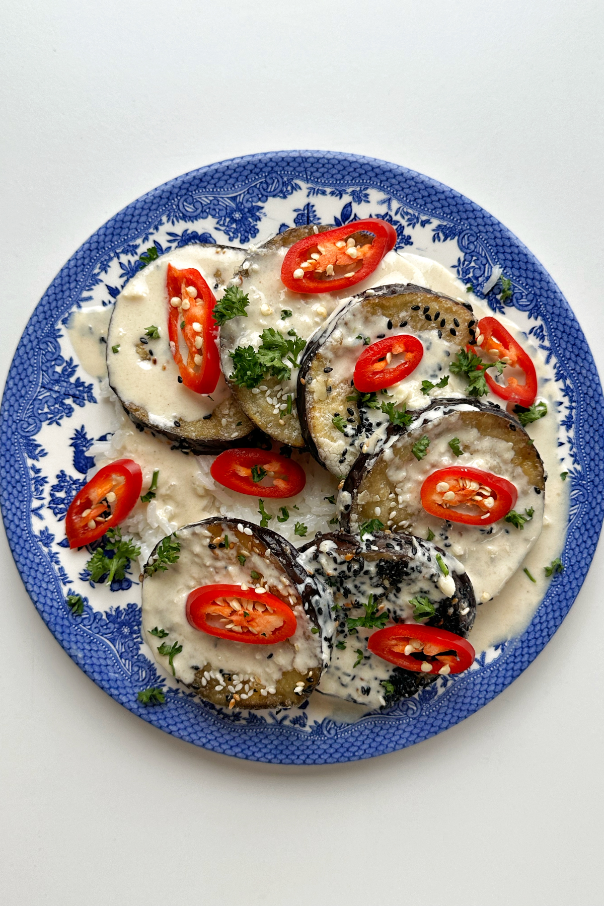 A blue plate topped with aubergine discs, red chillies, and parsley.