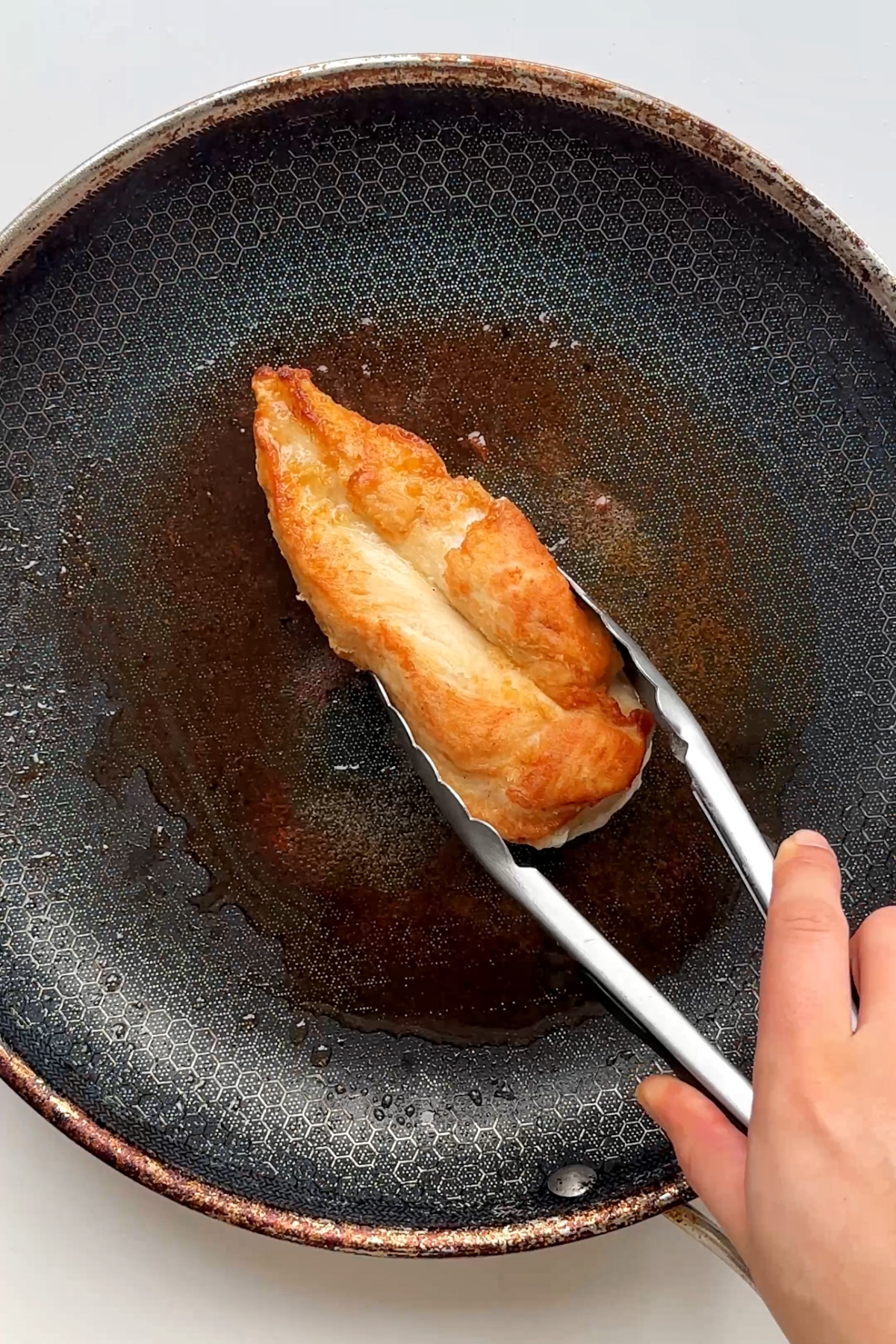 Frying a chicken breast in a black frying pan. 