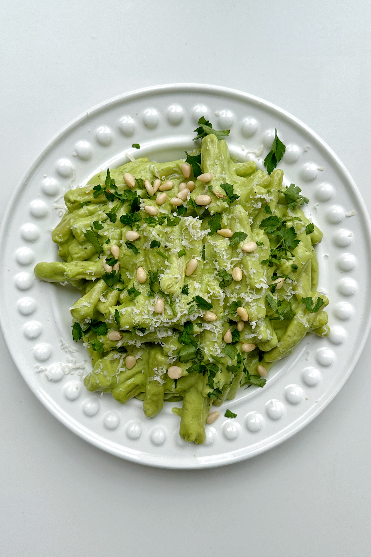 Avocado pesto pasta on a white plate topped with pine nuts.