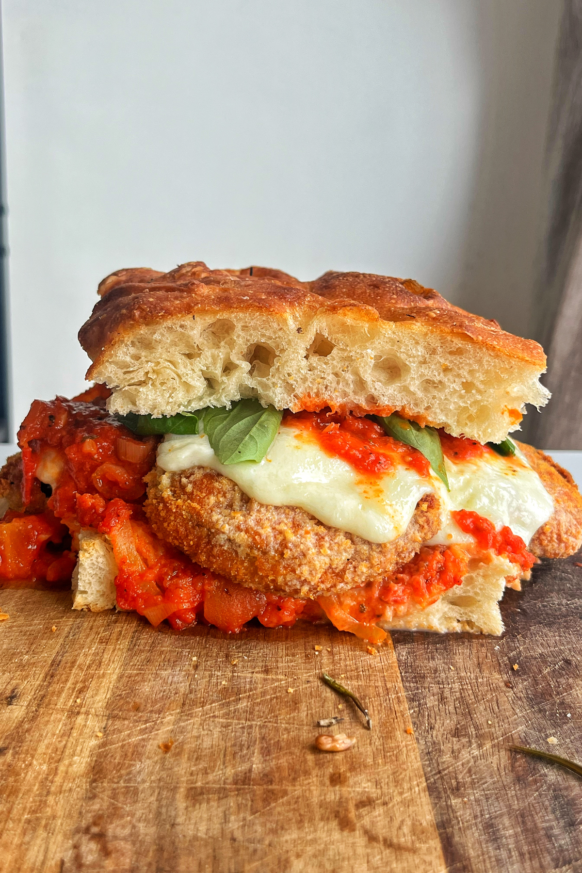 Sandwich with crispy eggplant, mozzarella, and marinara sauce on a chopping board.