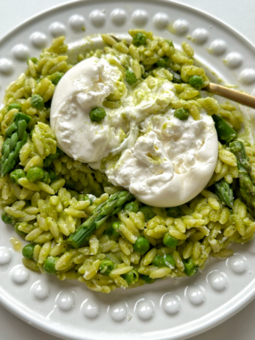 Close up of pea and asparagus orzo with burrata on top on a white plate.