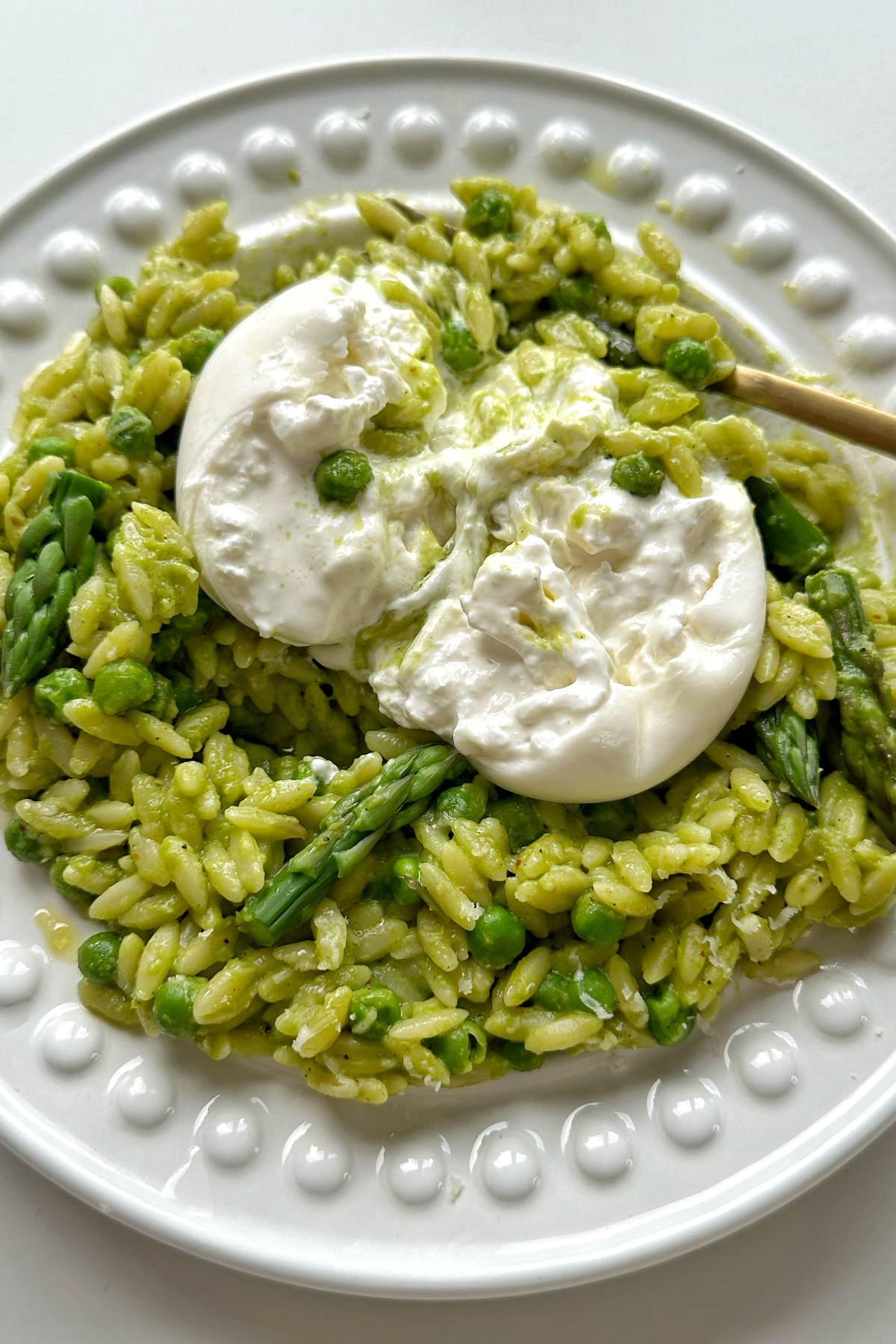 Close up of pea and asparagus orzo with burrata on top on a white plate.